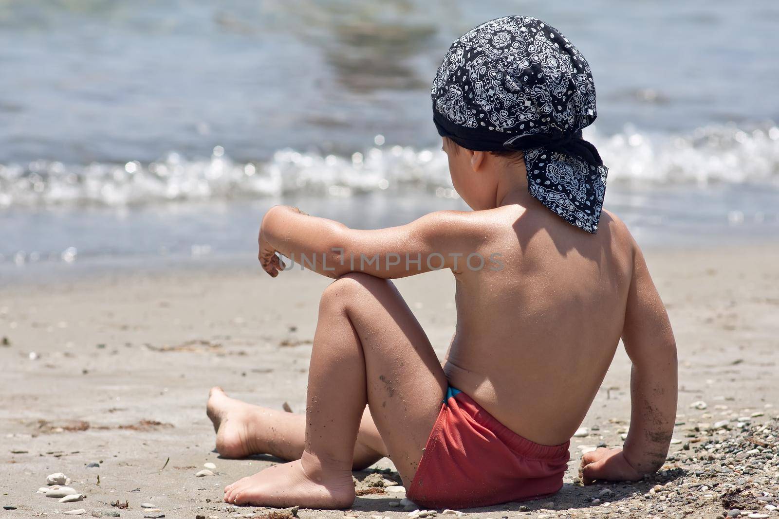 Little boy sitting on a beach looking on the waves