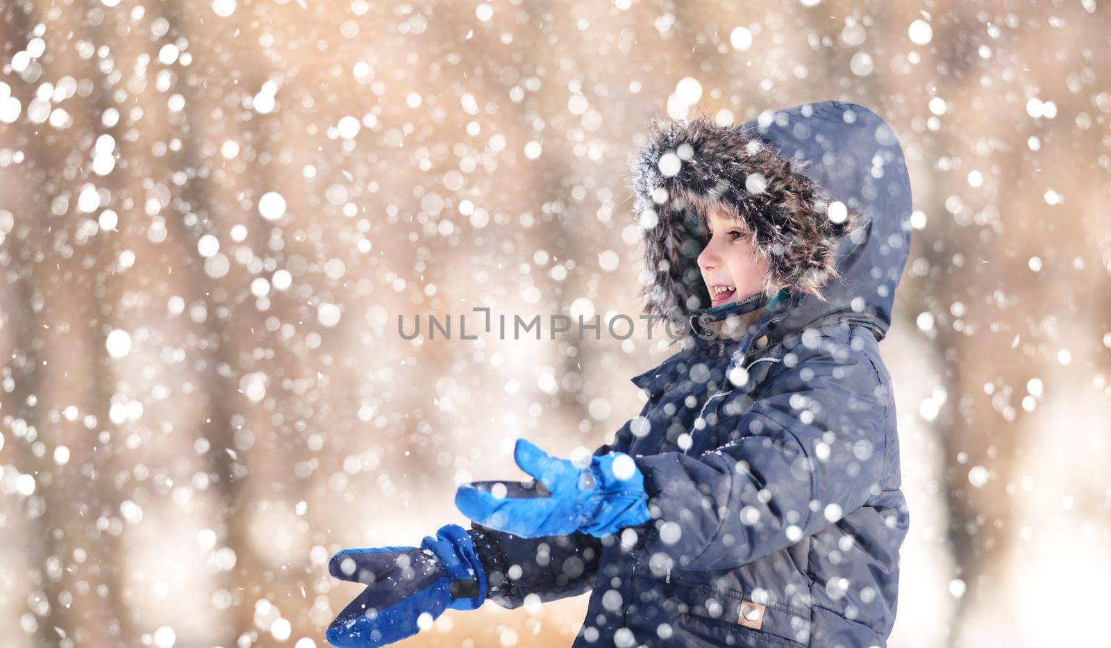 Cute boy playing with snow in the winter park  during a snowfall on a winter day