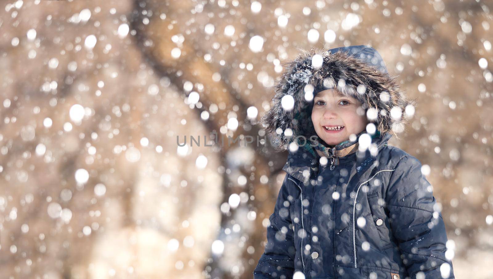 Cute boy playing with snow in the winter park  during a snowfall on a winter day