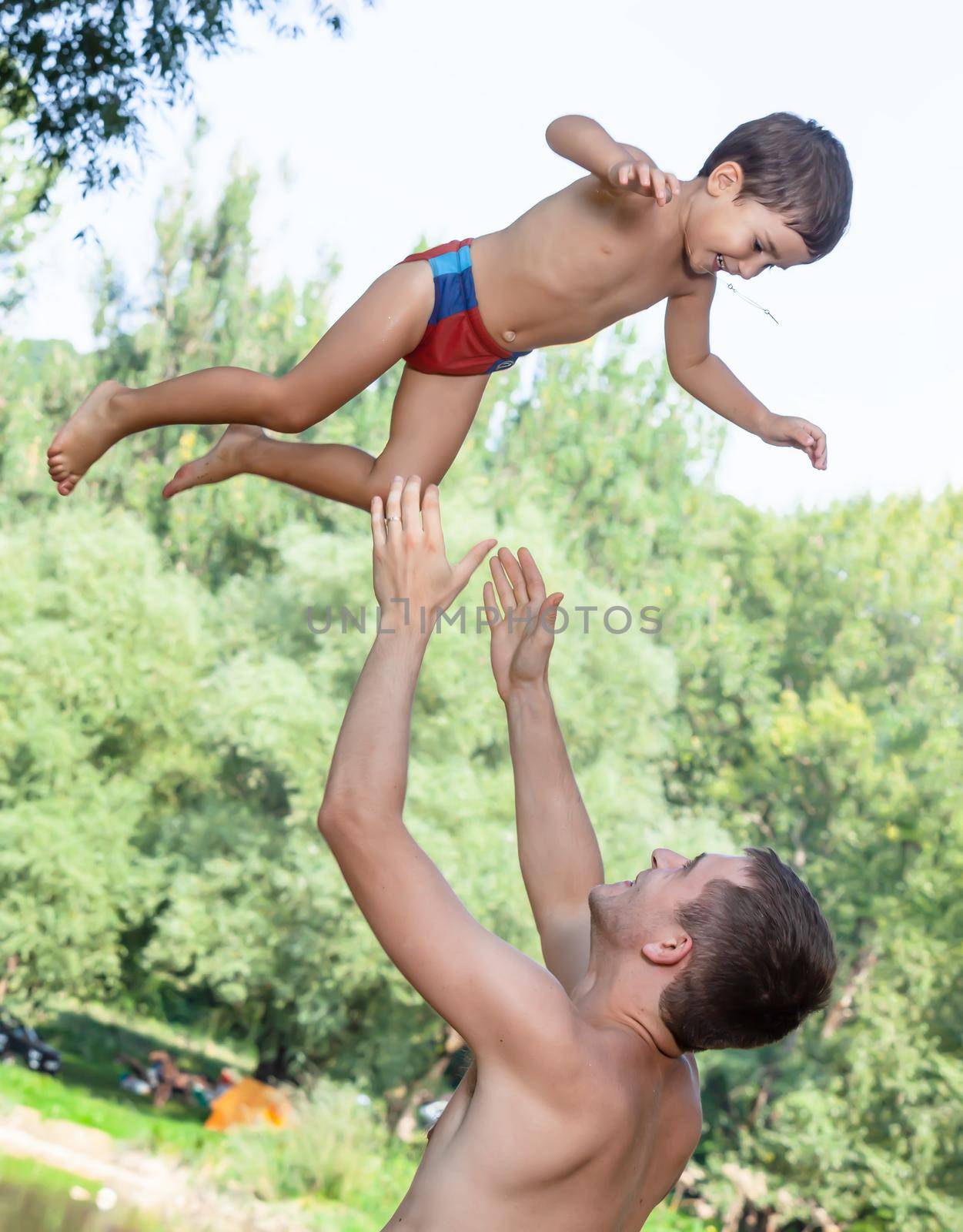 Happy childhood concept. Father throwing his child in the air. Loving father and his little son having fan together outdoors