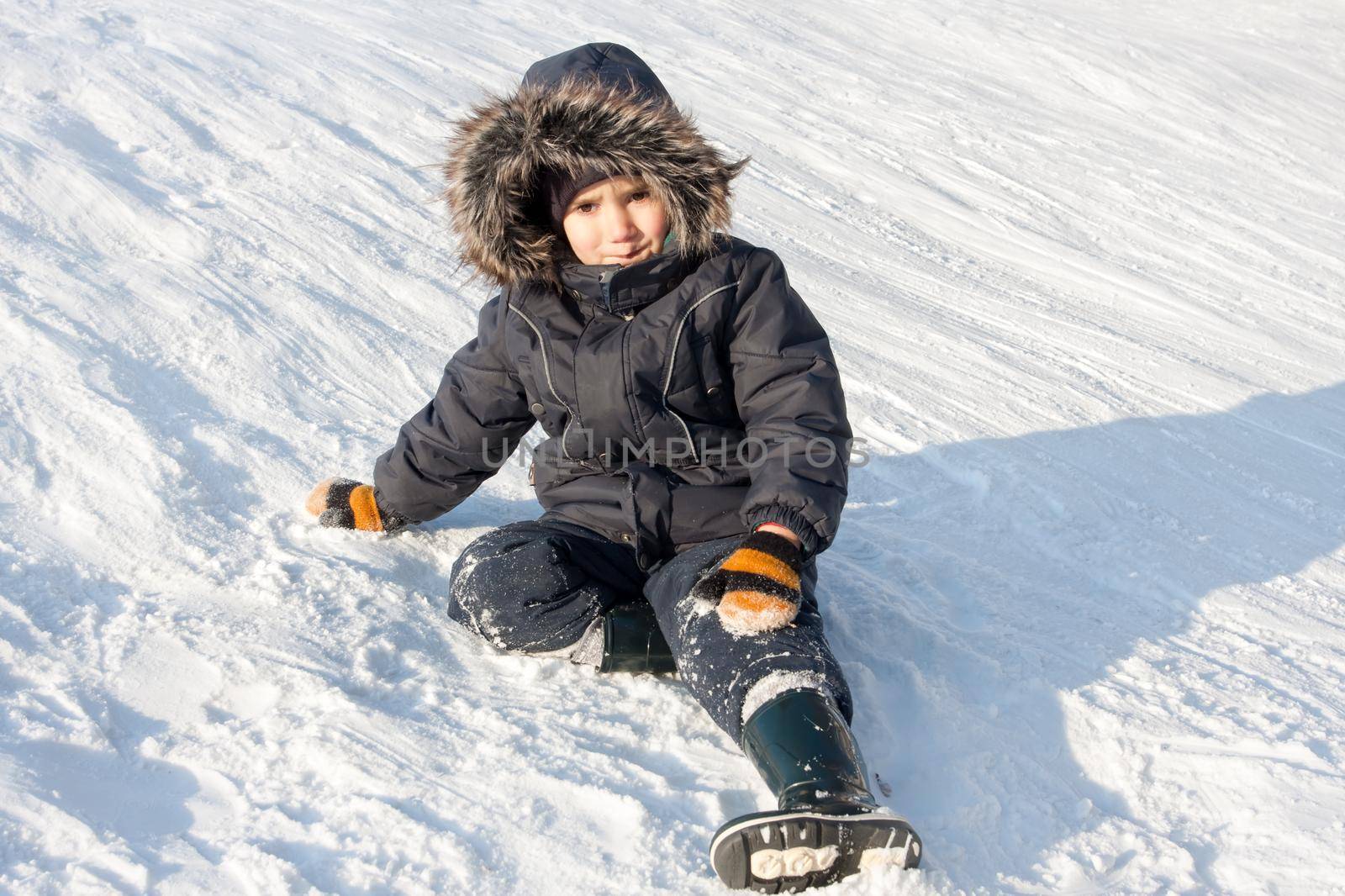 Young boy with tense emotions on face sitting on the snow