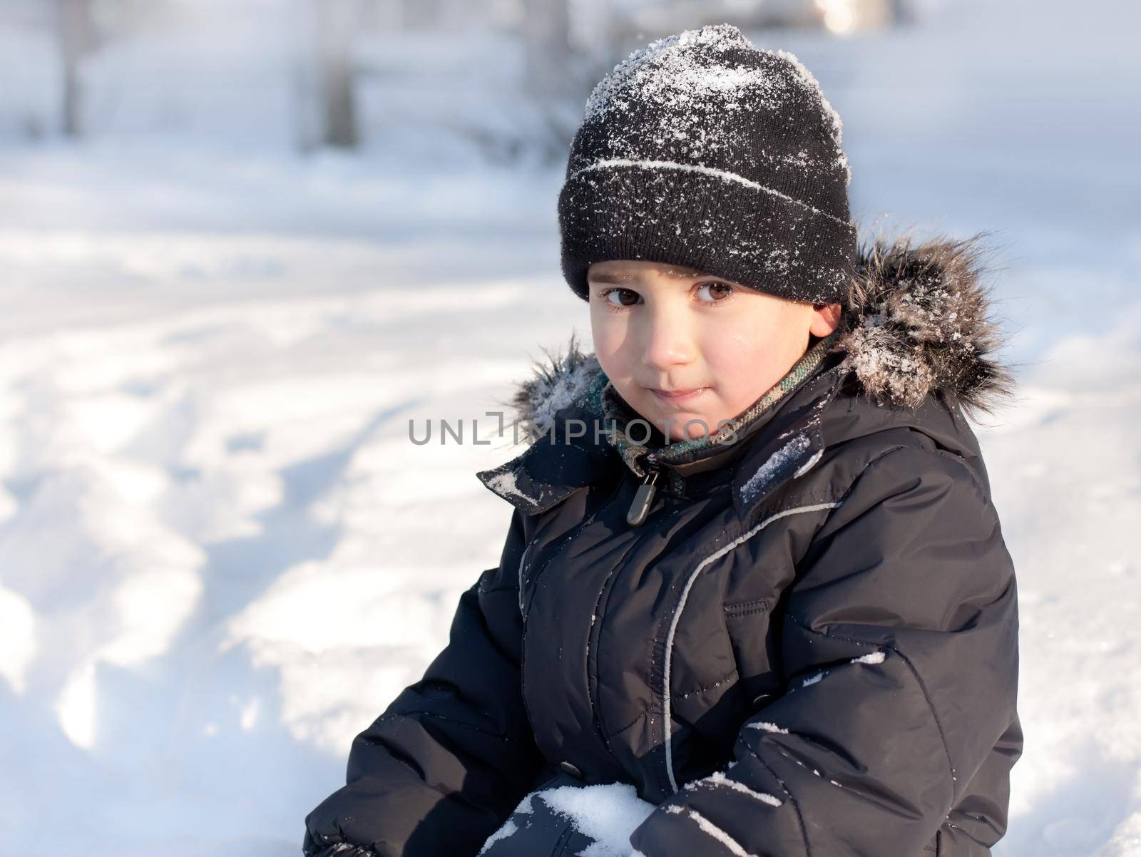 Winter portrait of young cute boy in furry hood and snowy hat