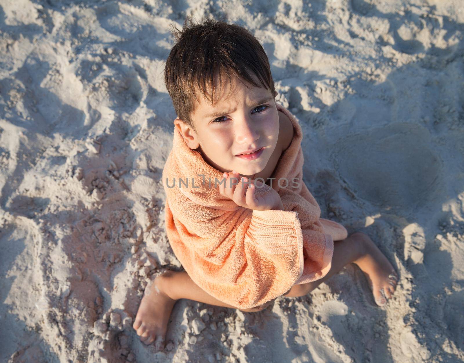 little boy wrapped in towel sitting on sandy beach by palinchak