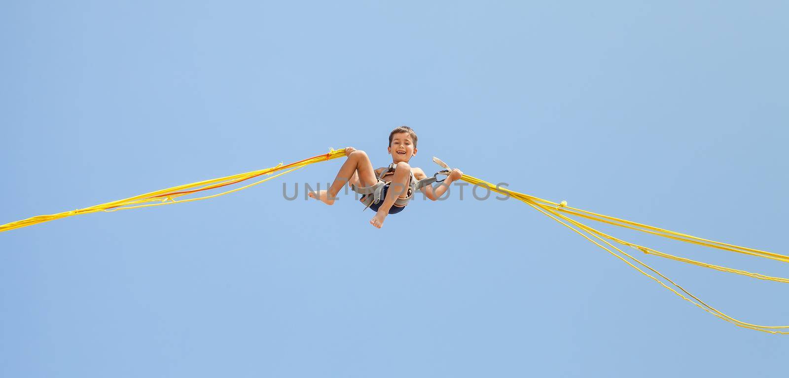 Little boy jumping on a trampoline on blue sky background 