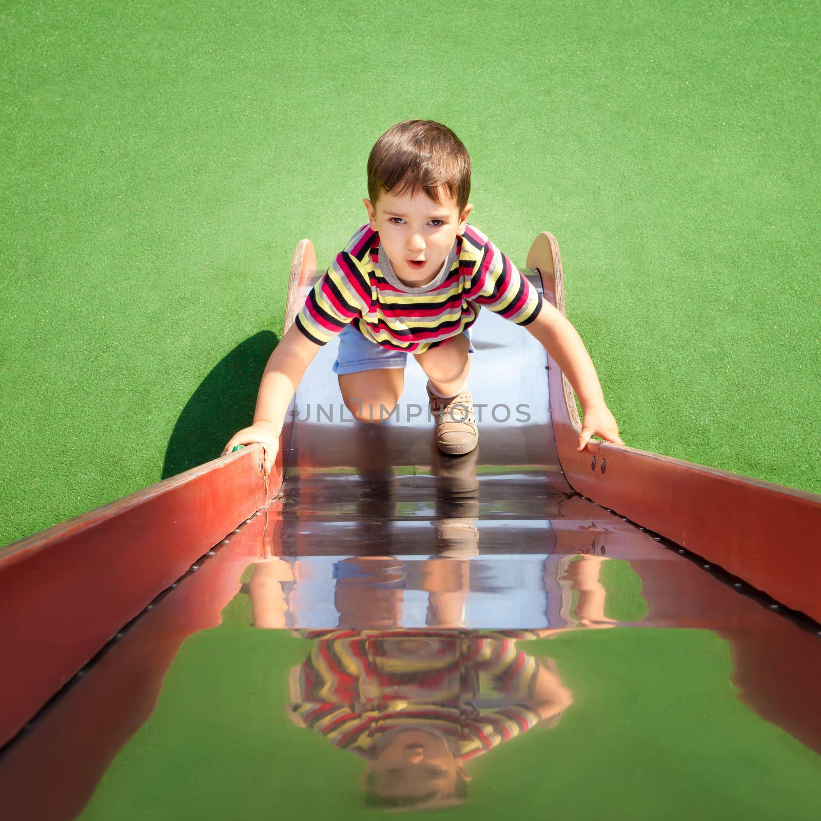 Cute young boy climbing up a slide on playground