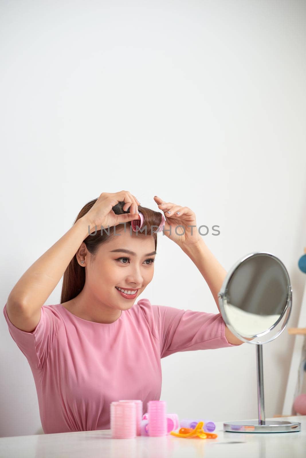 Beautiful woman with curlers smiling into mirror, enjoying her look, beauty