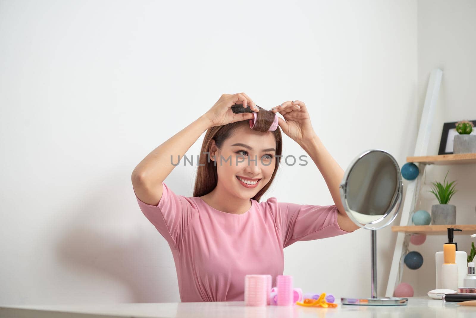 Beautiful woman with curlers smiling into mirror, enjoying her look, beauty by makidotvn