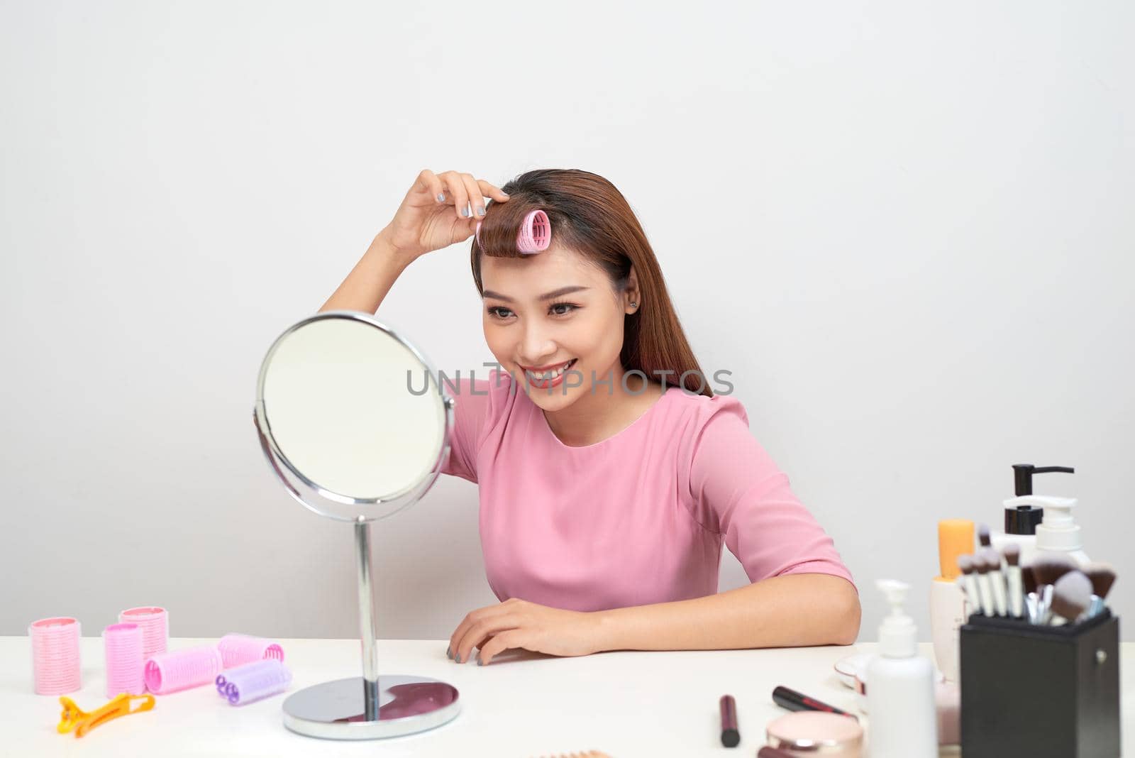 Beautiful woman with curlers smiling into mirror, enjoying her look, beauty by makidotvn