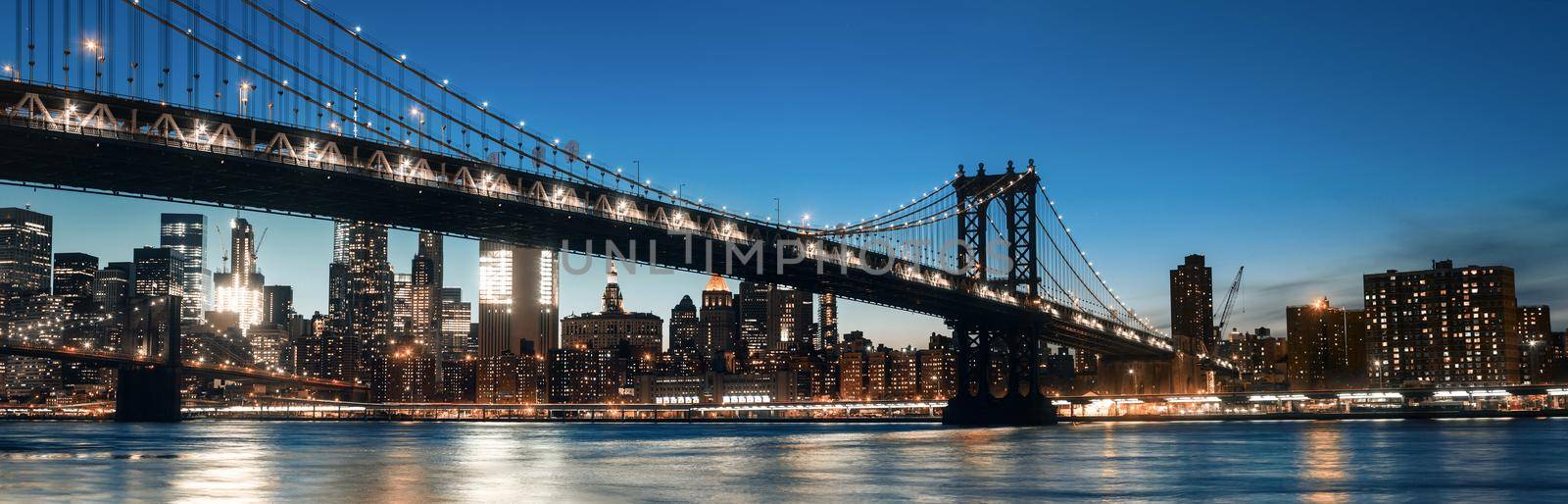 Manhattan Skyline and Manhattan Bridge At Night. Manhattan Bridge is a suspension bridge that crosses the East River in New York City. 