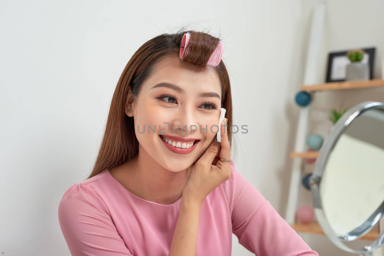 Cosmetic beauty procedures and makeover concept. Woman in hair curlers beautiful young woman using cotton pads at home by makidotvn
