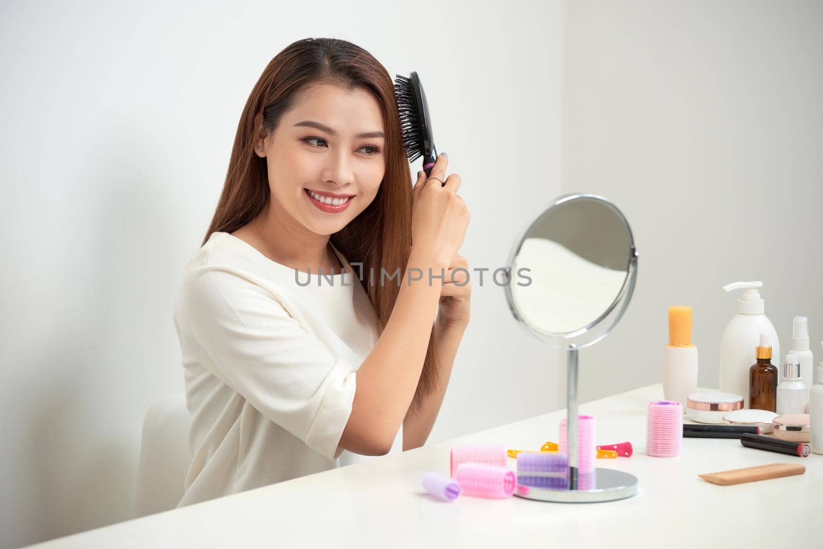 Getting rid of tangles. Beautiful young woman looking at her reflection in mirrorand brushing her long hair while sitting at the dressing table by makidotvn