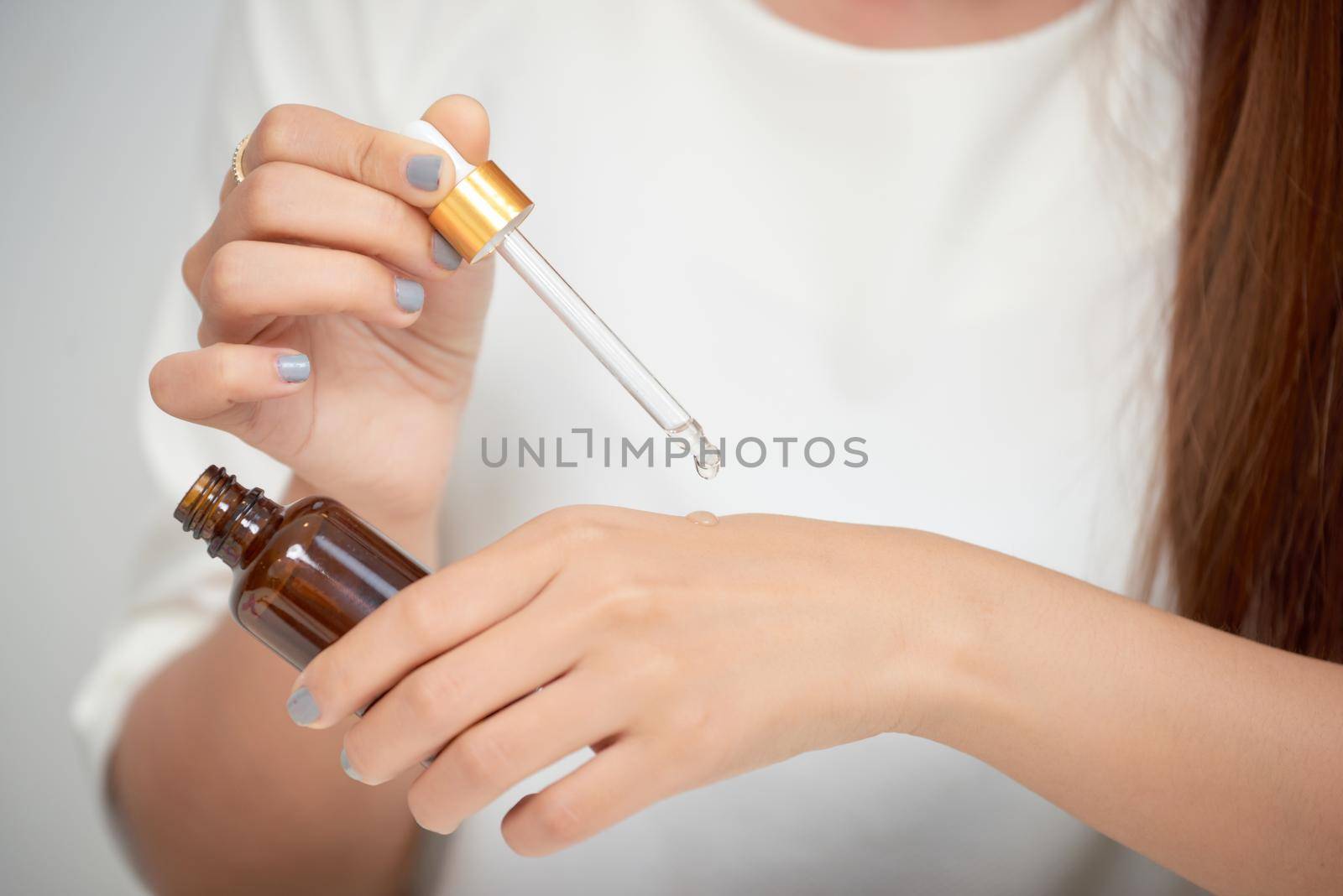 Pretty Caucasian woman putting cosmetic serum on her hand while sitting at the dressing table.