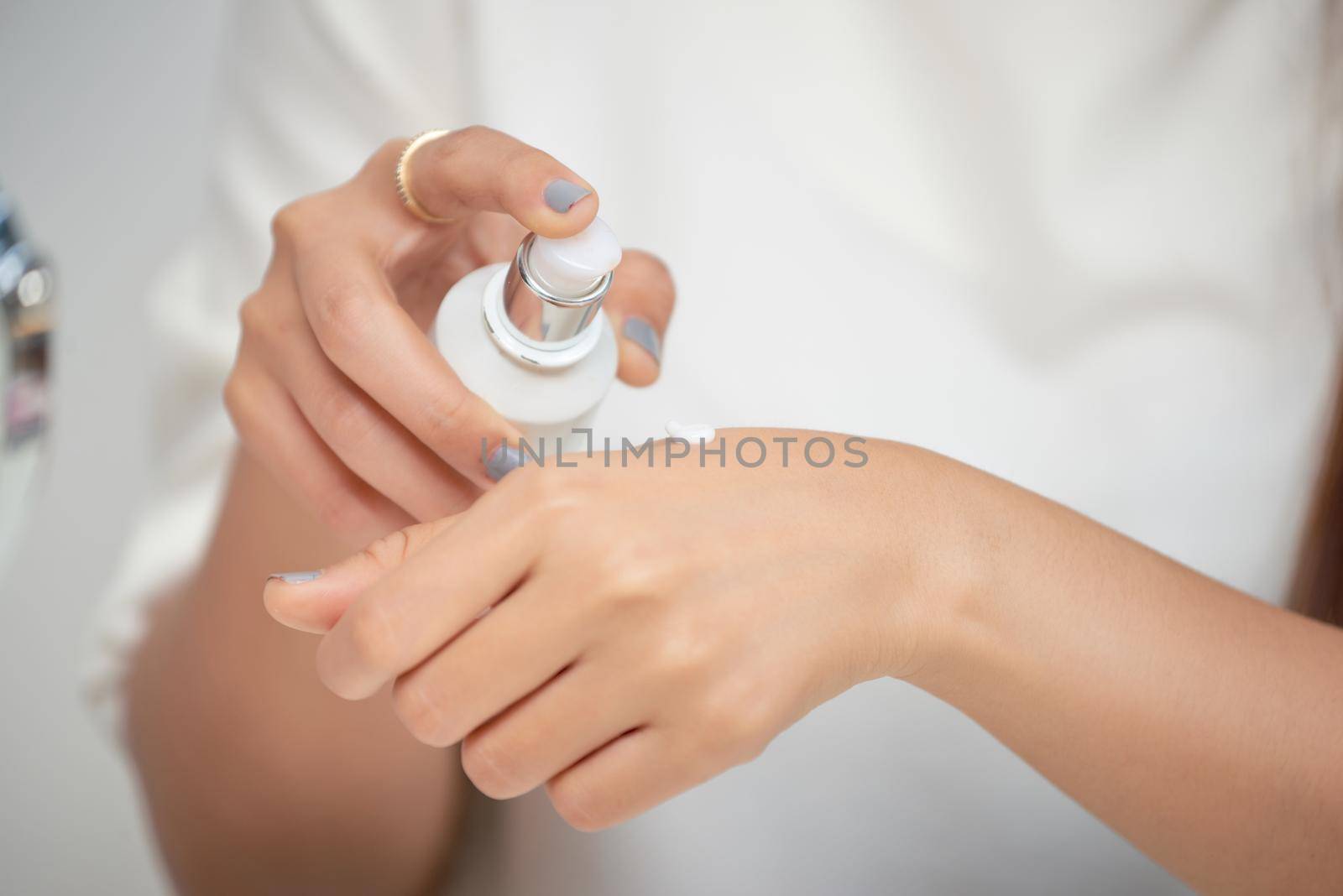 Young woman putting cream on the hand with smile while sitting at the dressing table by makidotvn