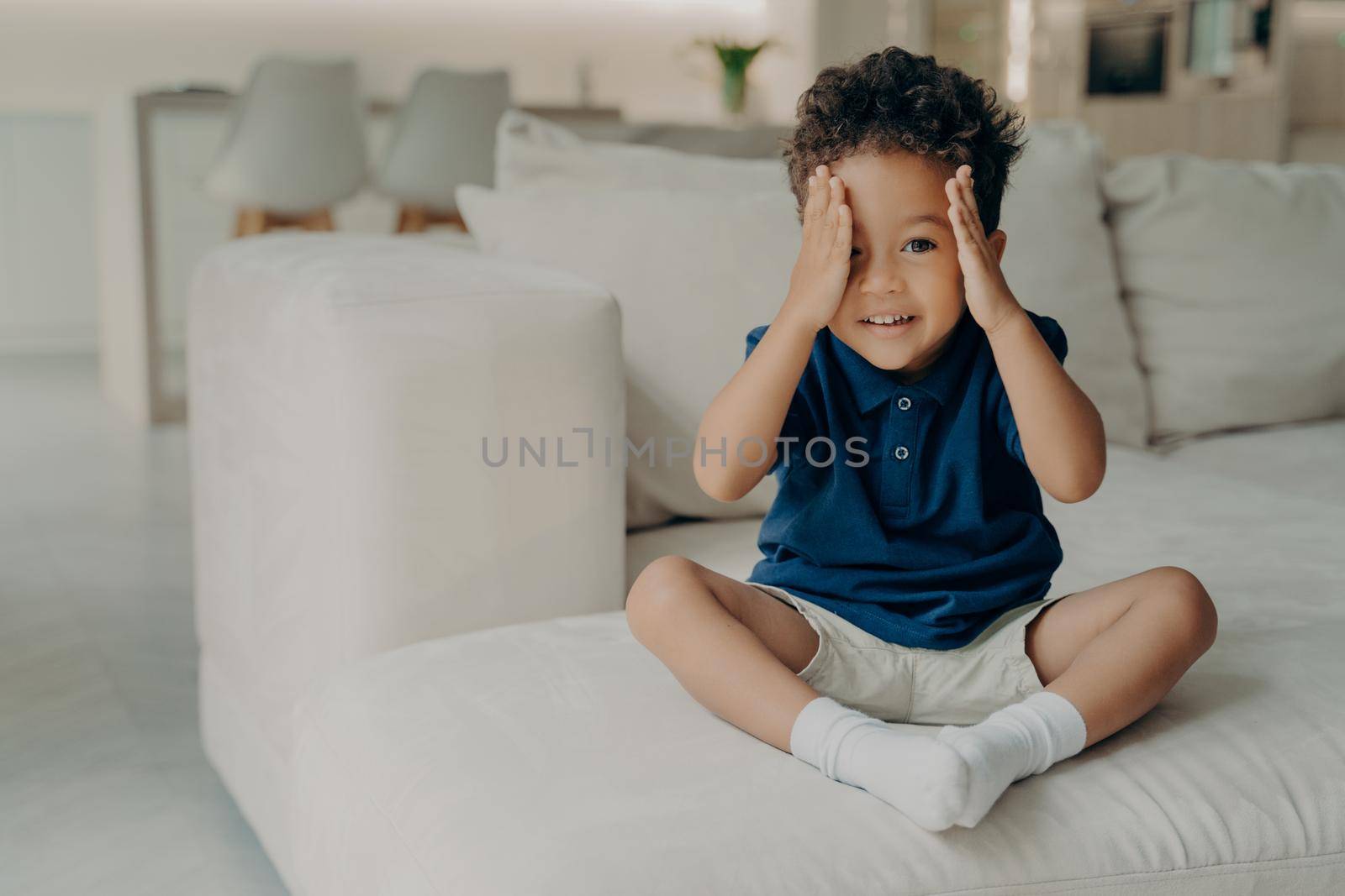 Cute little boy with curly hair enjoying game of hide and seek at home by vkstock