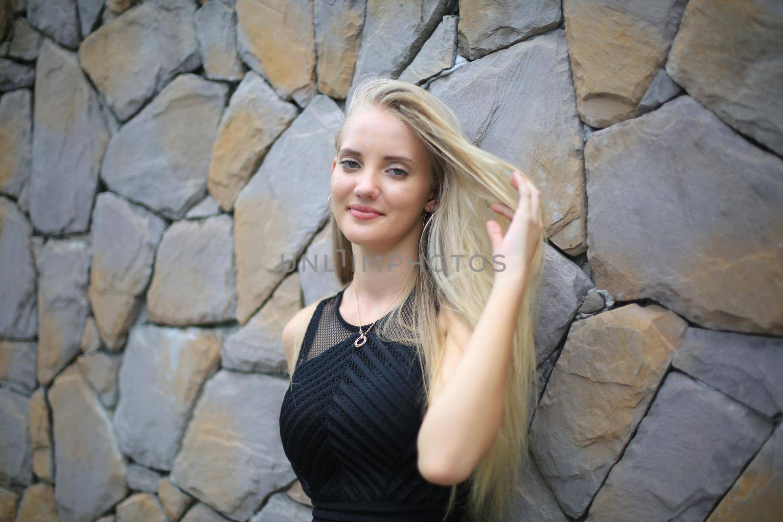 Portrait of Beautiful blonde hair girl on black dress against stone wall as fashion portrait outdoor. by chuanchai