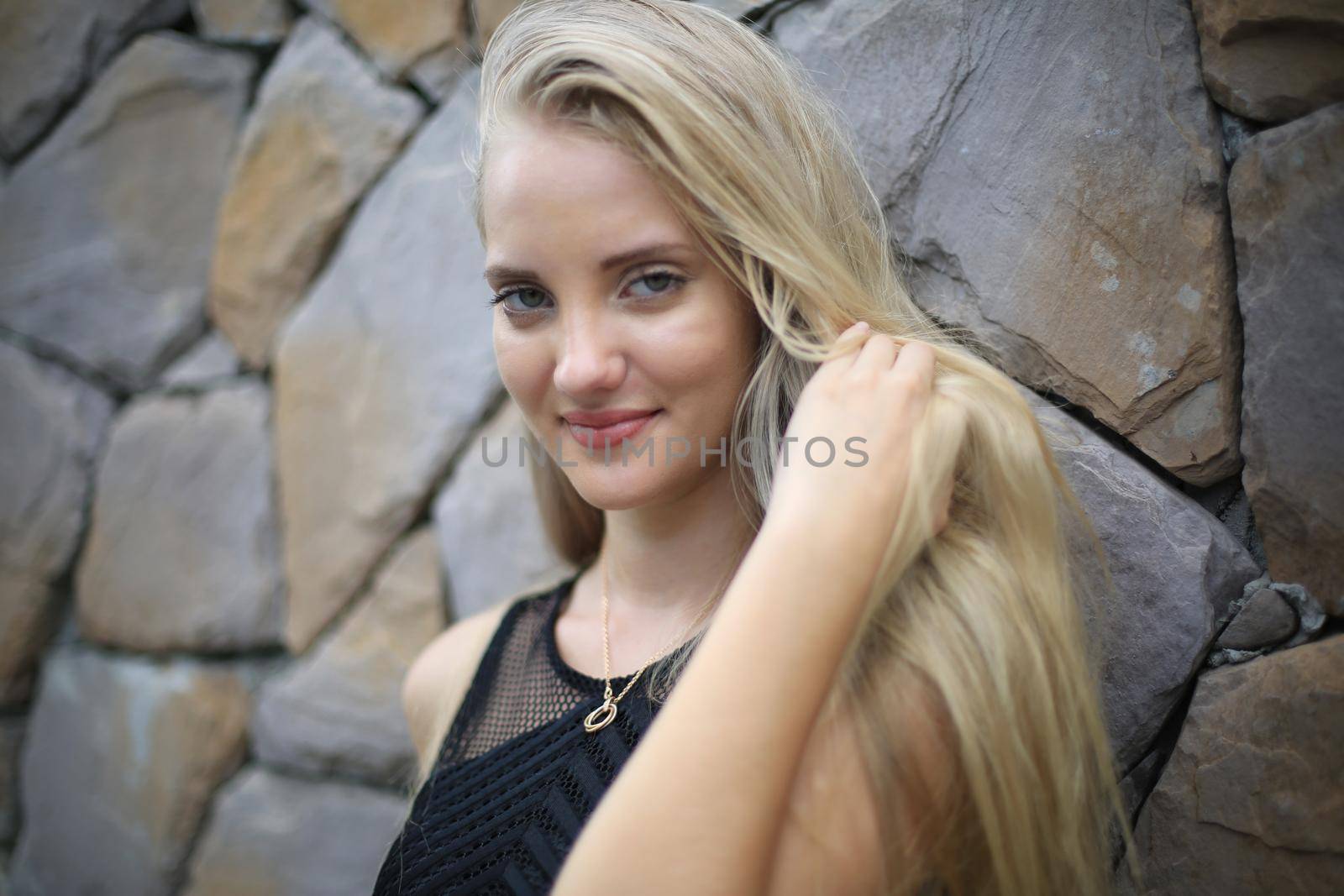 Portrait of Beautiful blonde hair girl on black dress against stone wall as fashion portrait outdoor.