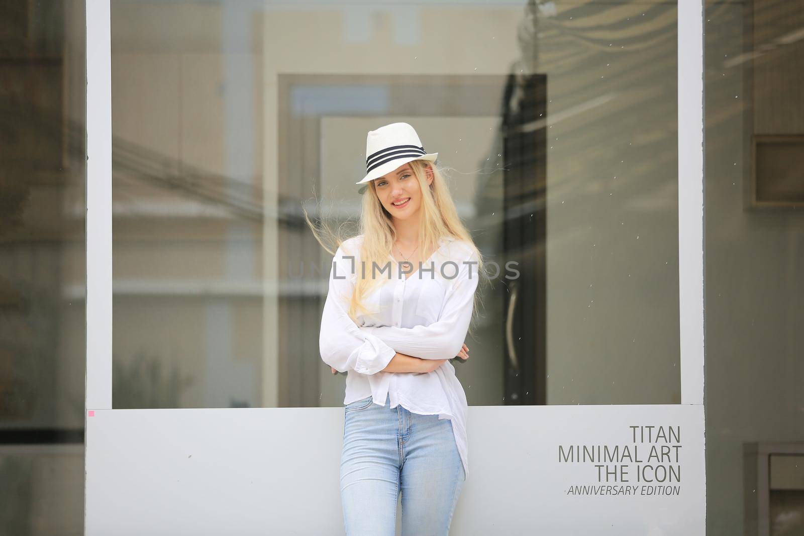 Beautiful blonde hair girl with white hat standing against wall glass as fashion pose outdoor. by chuanchai