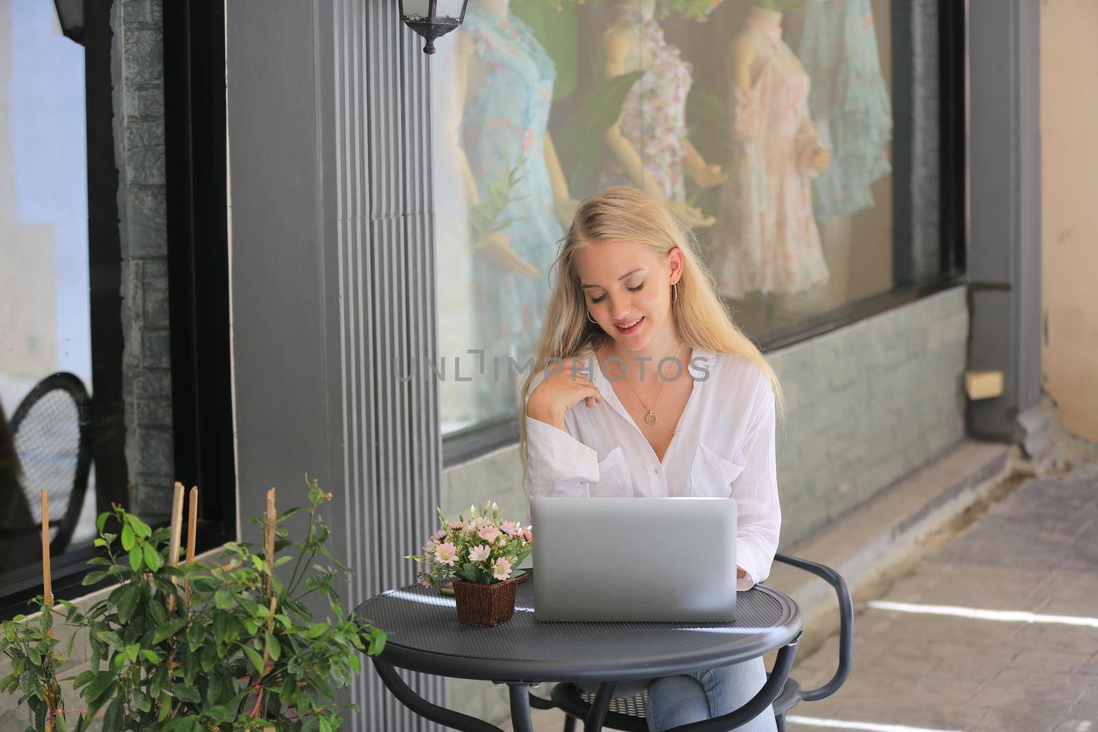 Beautiful blonde hair girl sitting with laptop in front of retails shop,Small business owner concept