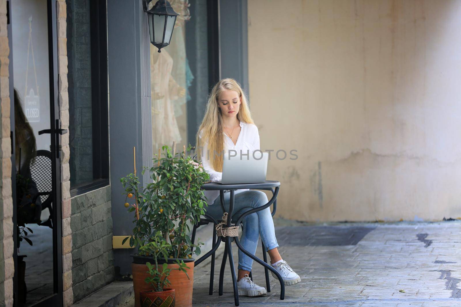 Beautiful blonde hair girl sitting with laptop in front of retails shop,Small business owner concept by chuanchai