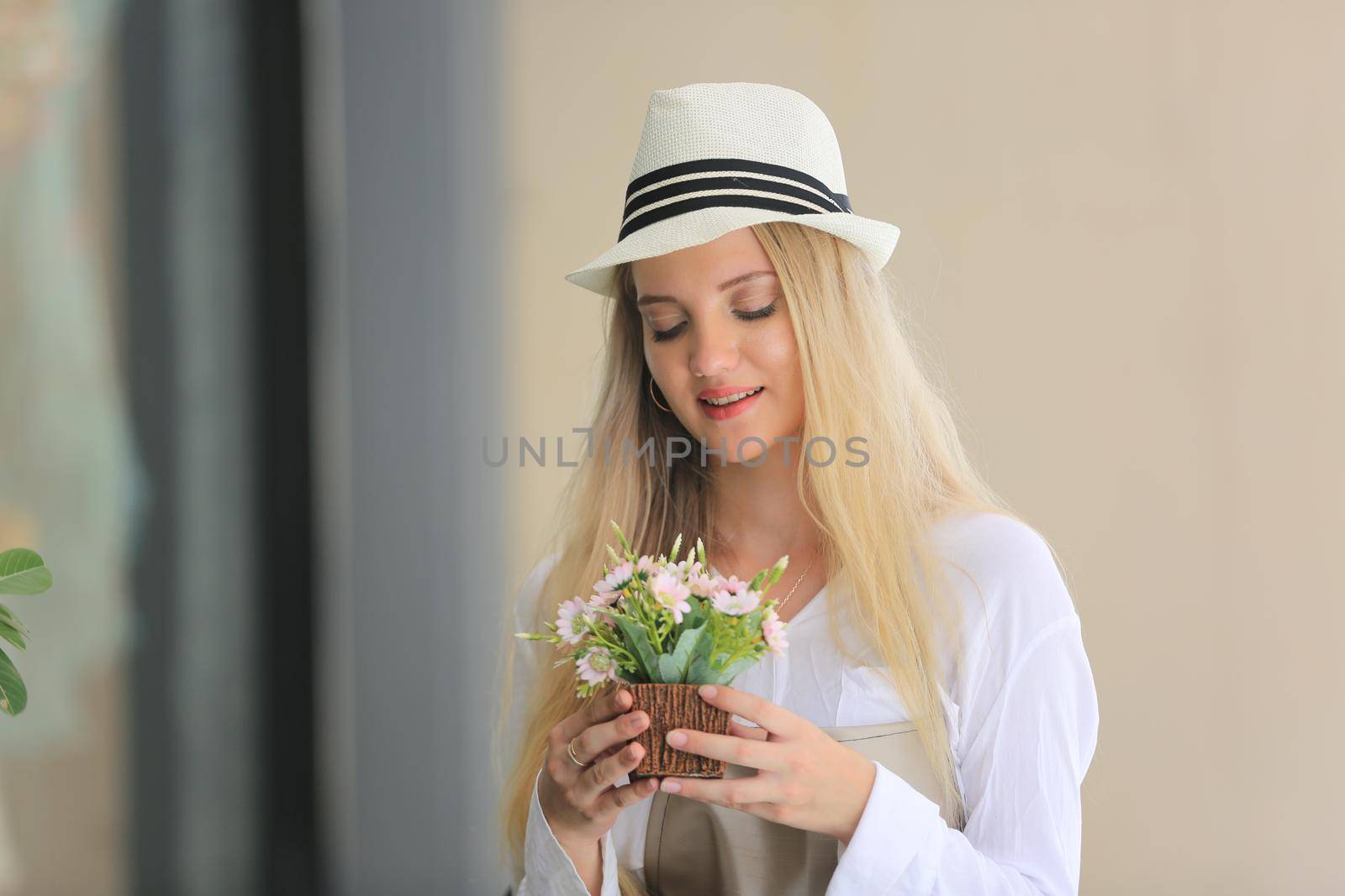 Beautiful blonde hair girl standing with confidence in front of flower in open retails flora shop. Small business owner concept.