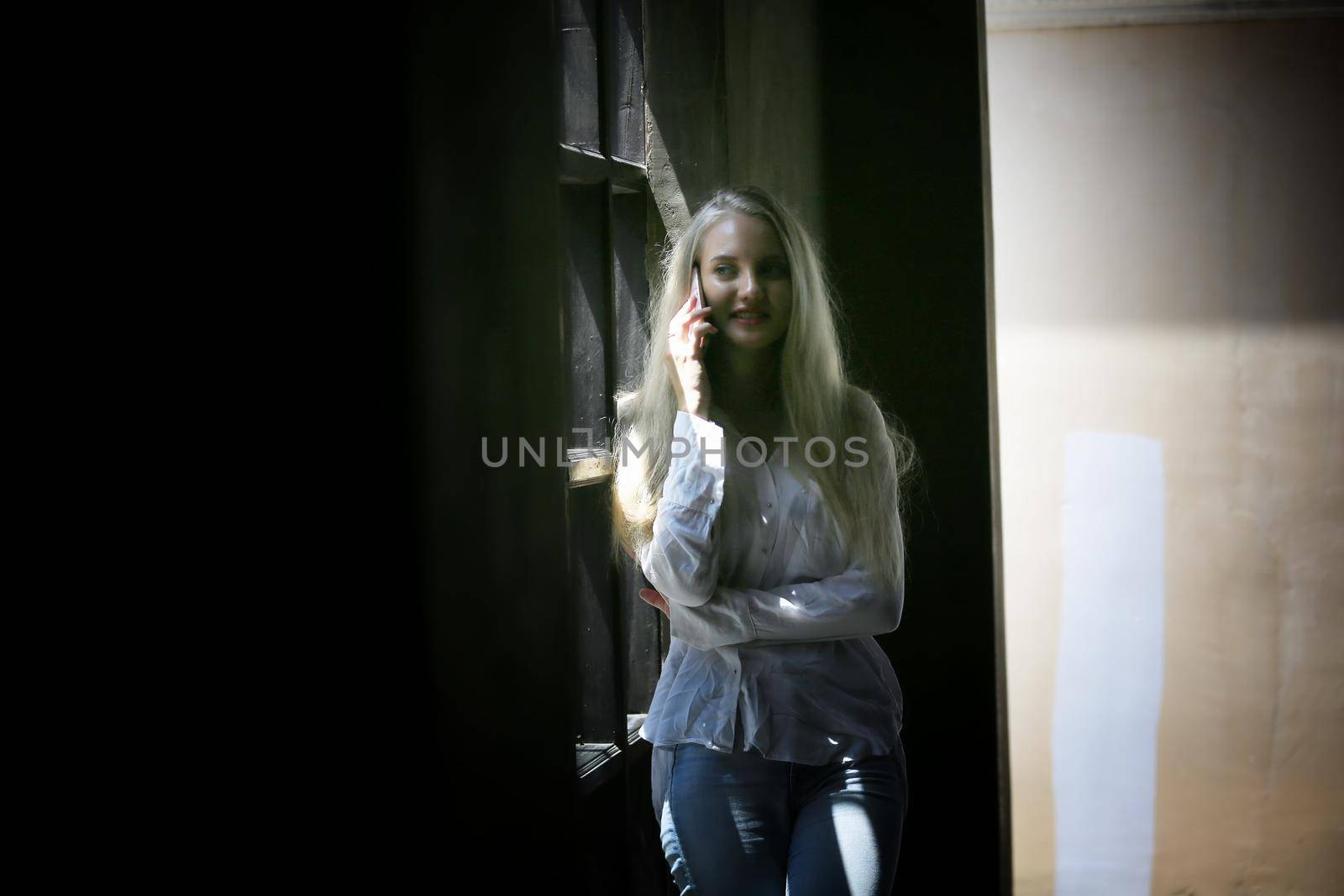 Beautiful blonde hair girl speaking on mobile phone with laptop on table outside coffee shop. by chuanchai