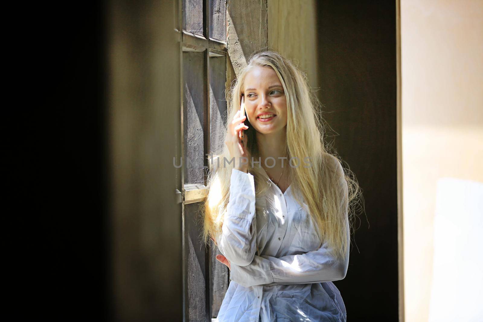 Beautiful blonde hair girl speaking on mobile phone with laptop on table outside coffee shop. by chuanchai