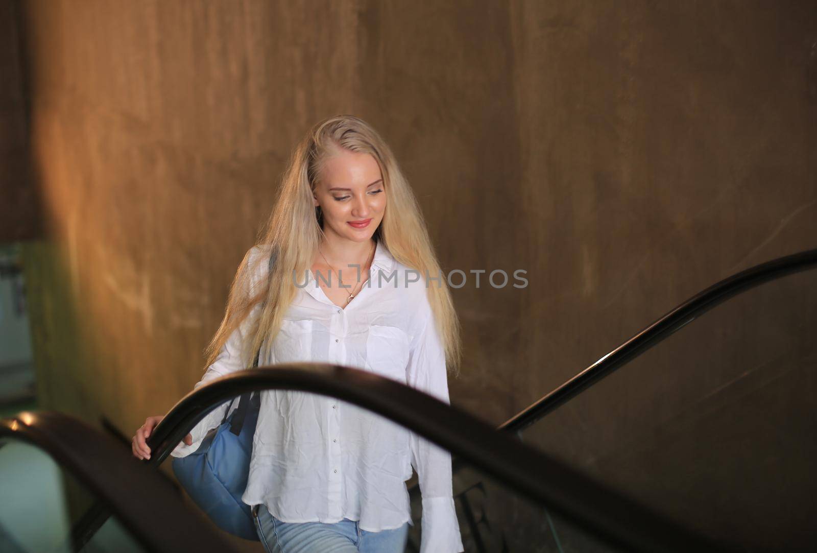 Beautiful blonde girl walking up the escalator.