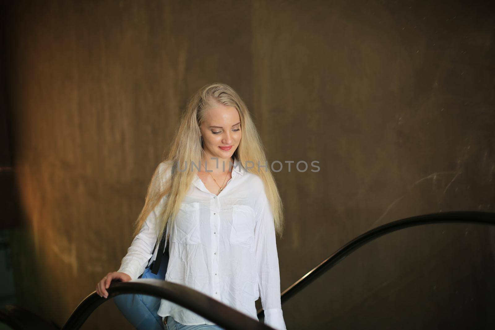 Beautiful blonde girl walking up the escalator.