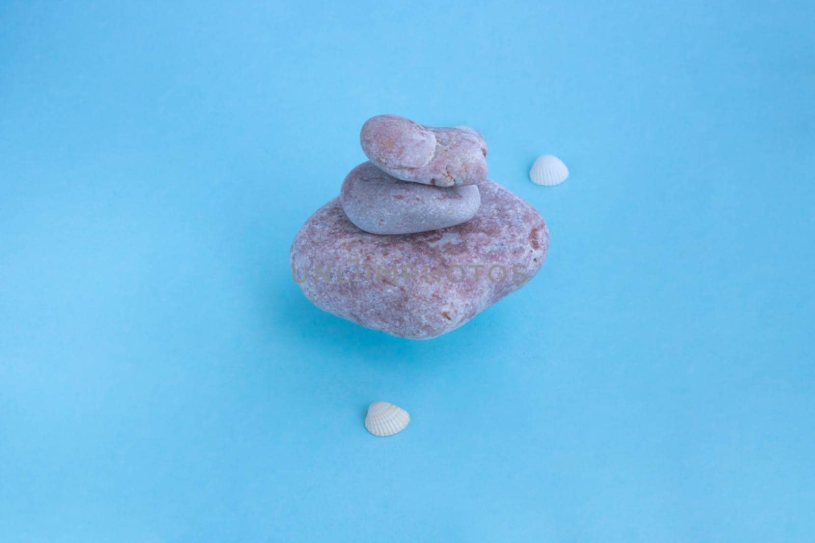 A stack of floating pink stones and small shells on a blue background. The concept of a relaxing massage for health.