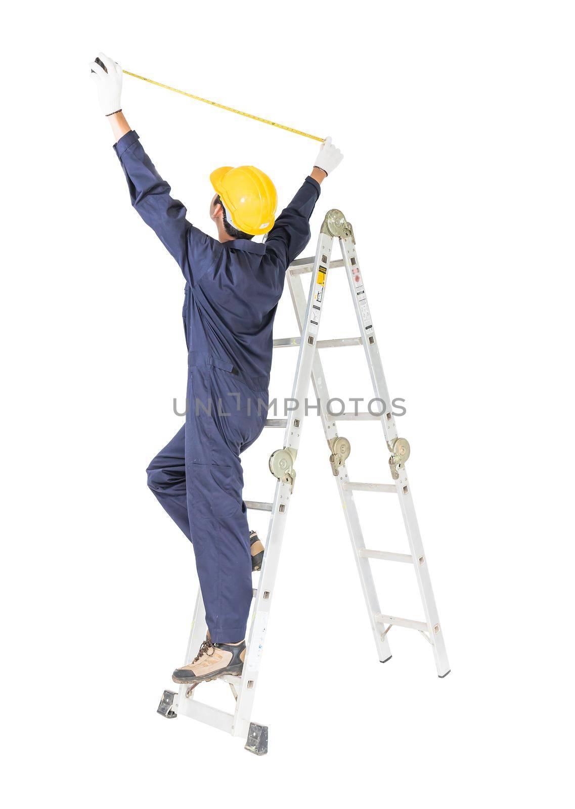 Young handyman in uniform standing on ladder while using tape measure on white, Cutout isolated on white background