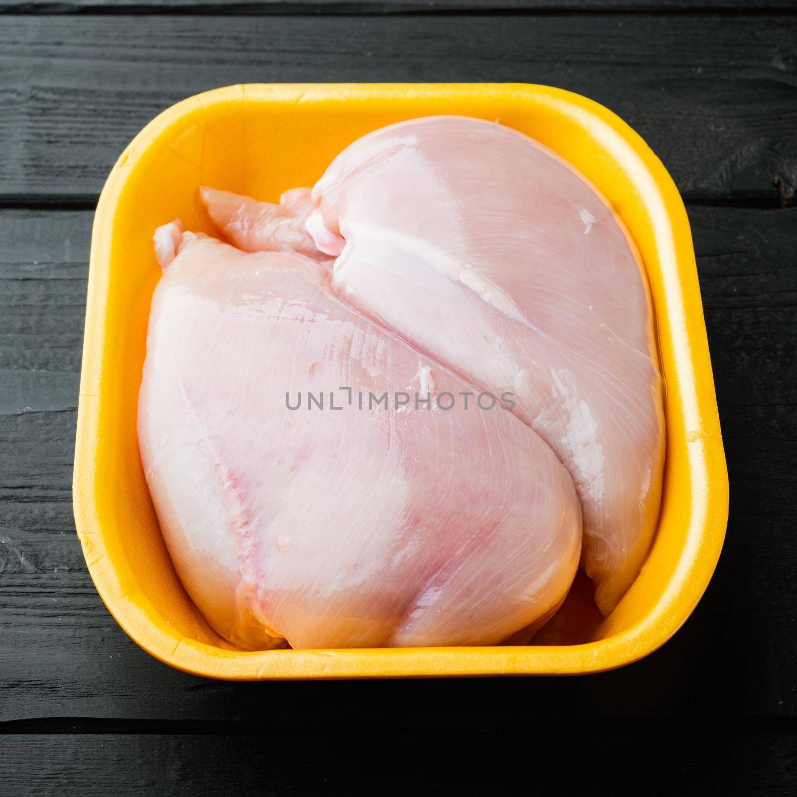 Raw chicken breast fillet in tray, on black wooden table by Ilianesolenyi