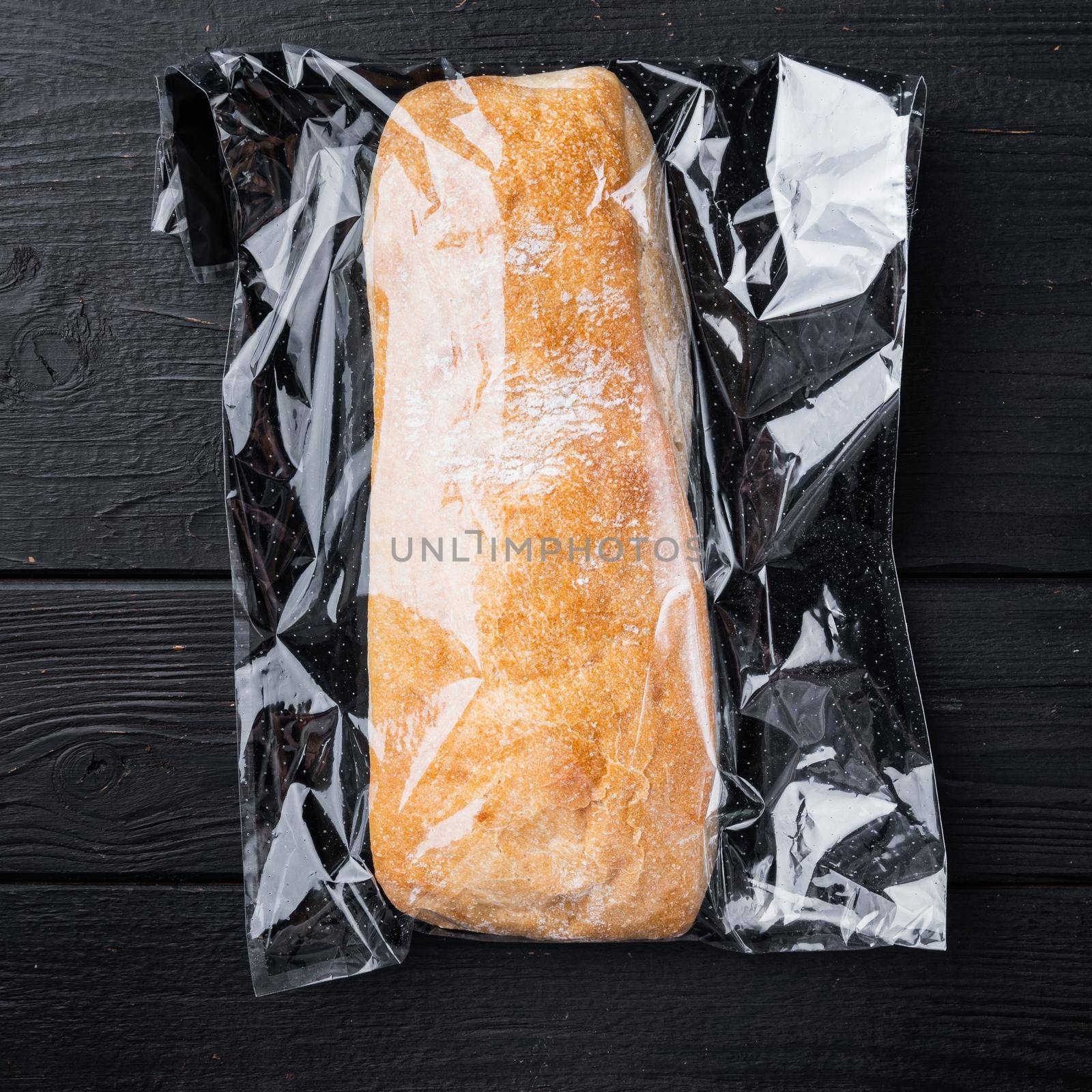 Ciabatta in plastic bag, on black wooden table background, top view flat lay by Ilianesolenyi