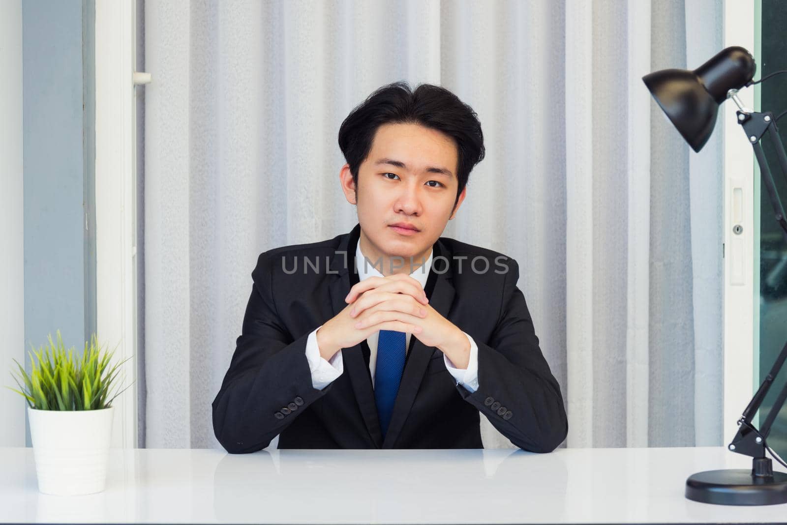 Work from home, Close up face of Asian young businessman video conference call or facetime he looking to camera sitting and holding hands to listen to colleagues explain the work on desk at office