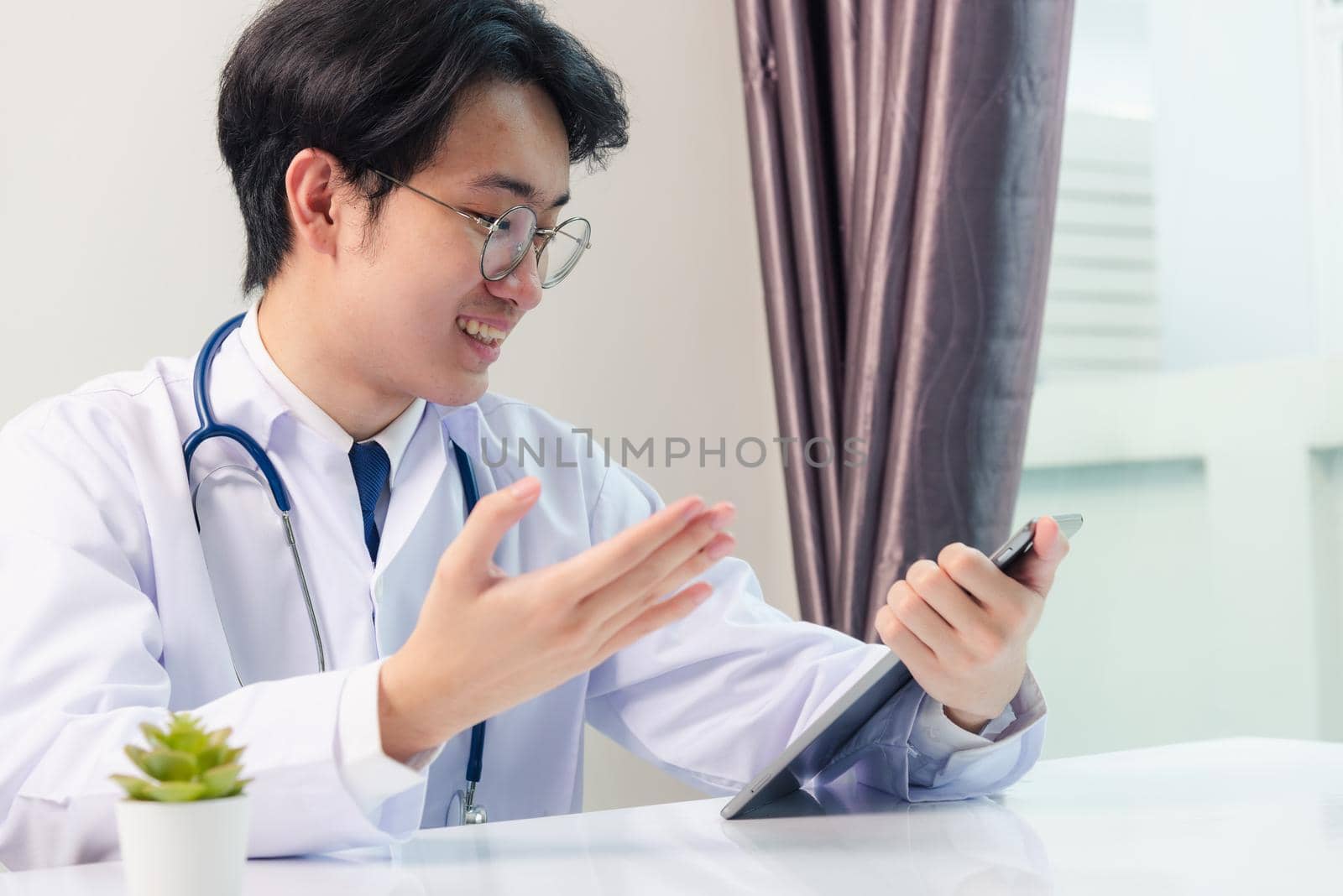 Happy Asian young doctor handsome man smile wear glasses use modern smart digital tablet computer explain patients symptoms of illness on desk at hospital office, Technology Healthcare And Medicine