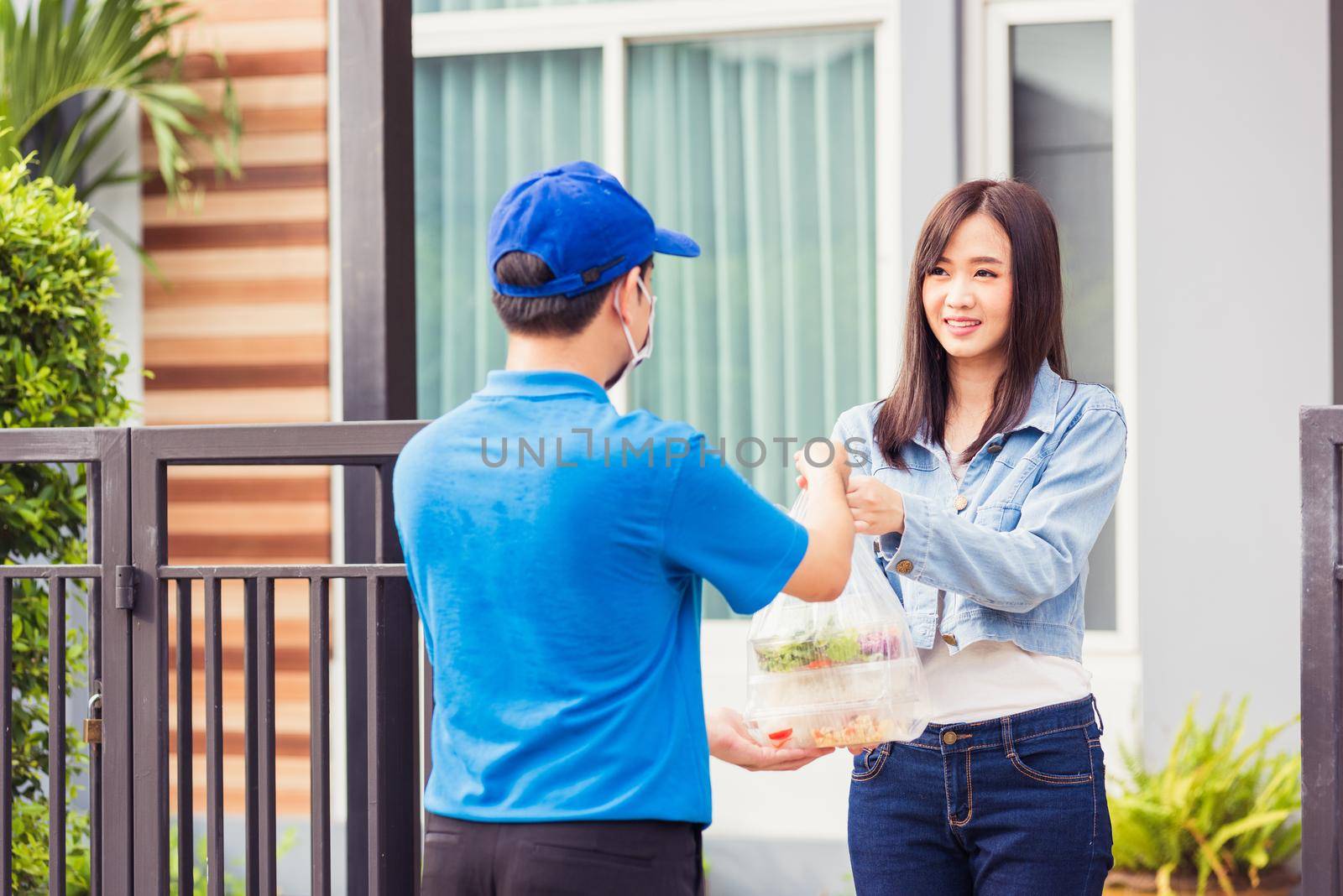 Asian young delivery man wear face mask he making grocery service giving rice food boxes plastic bags to woman customer receiving door at house after pandemic coronavirus, Back to new normal concept