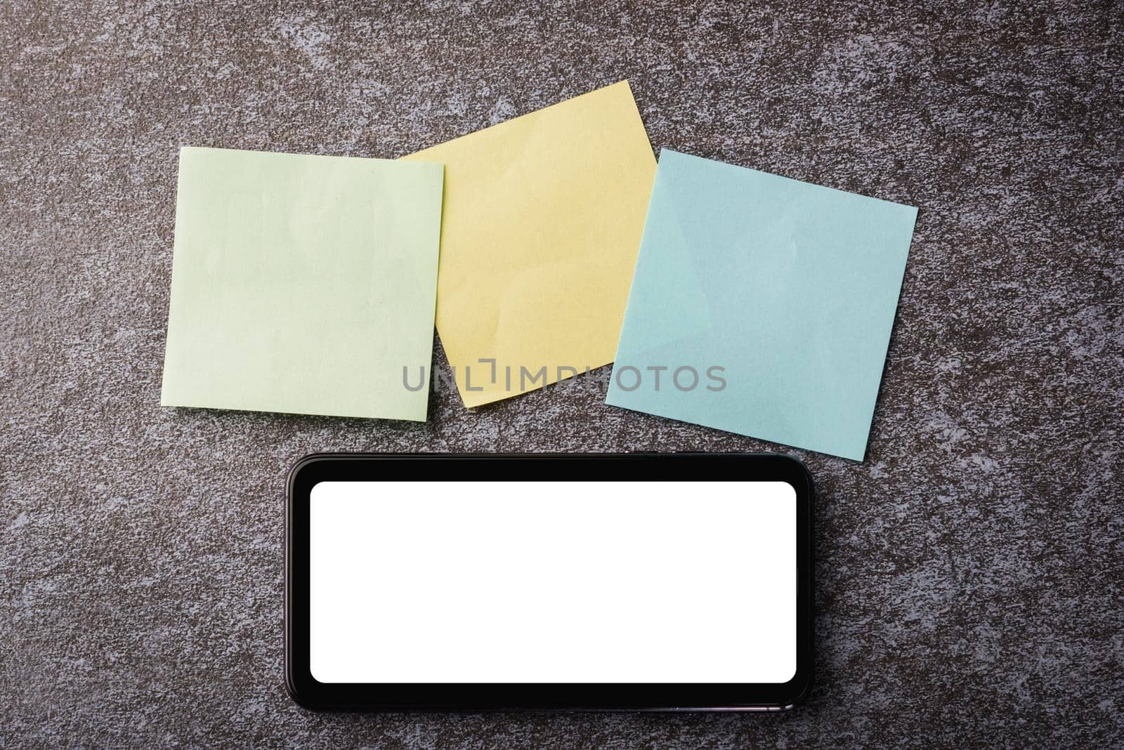 Above blank paper stick note list yellow, green and blue with the modern smart mobile phone blank screen on concrete background, Business reminder concept