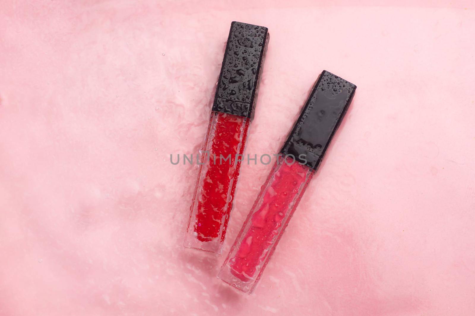 Lip gloss and water drops on a pink background. The concept of a bottle of lip gloss without labels. Cosmetology. Decorative cosmetics. Copy space