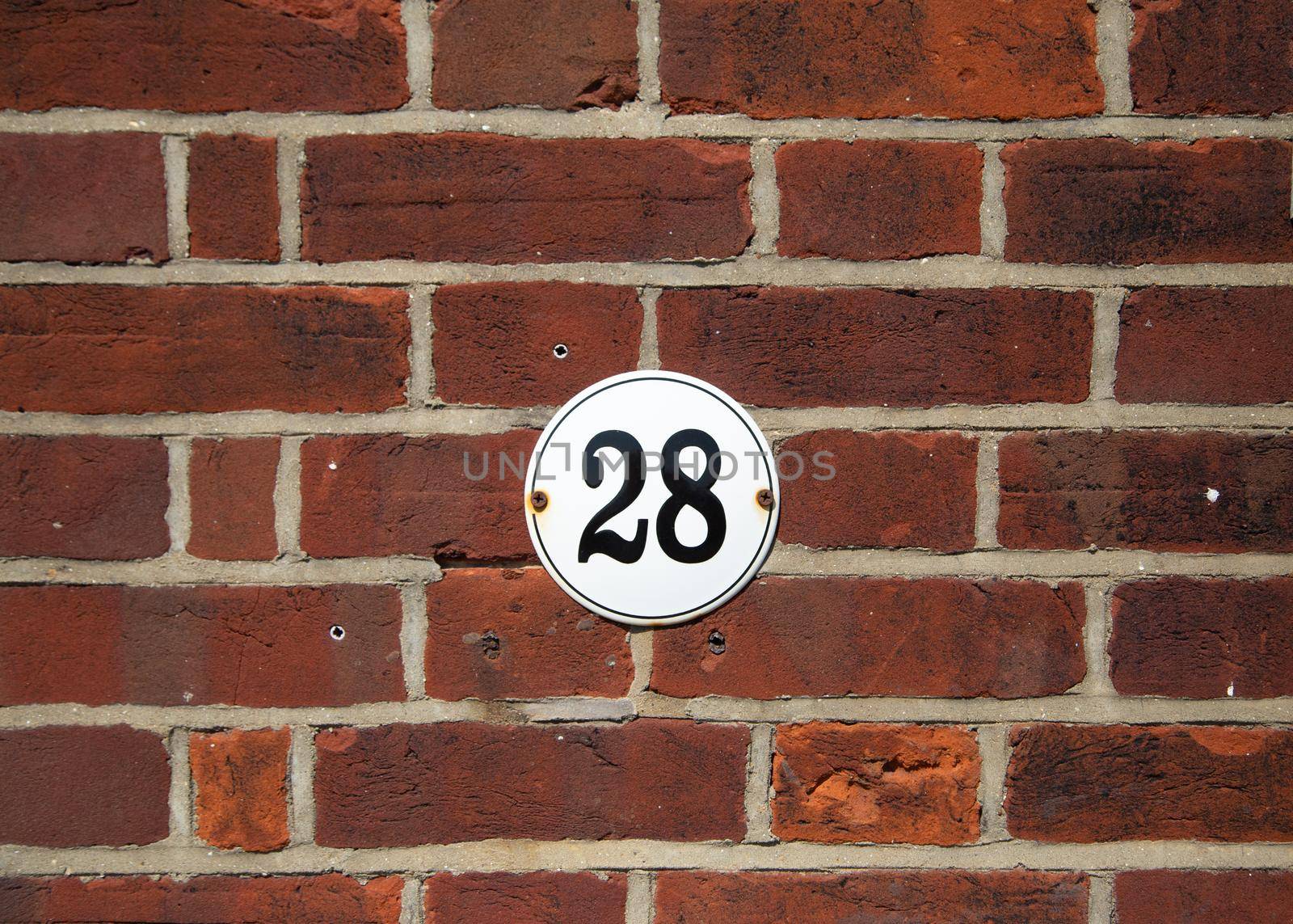 Number 28 on old red brick wall. Black number 28 on white round house plate. Antique UK house number