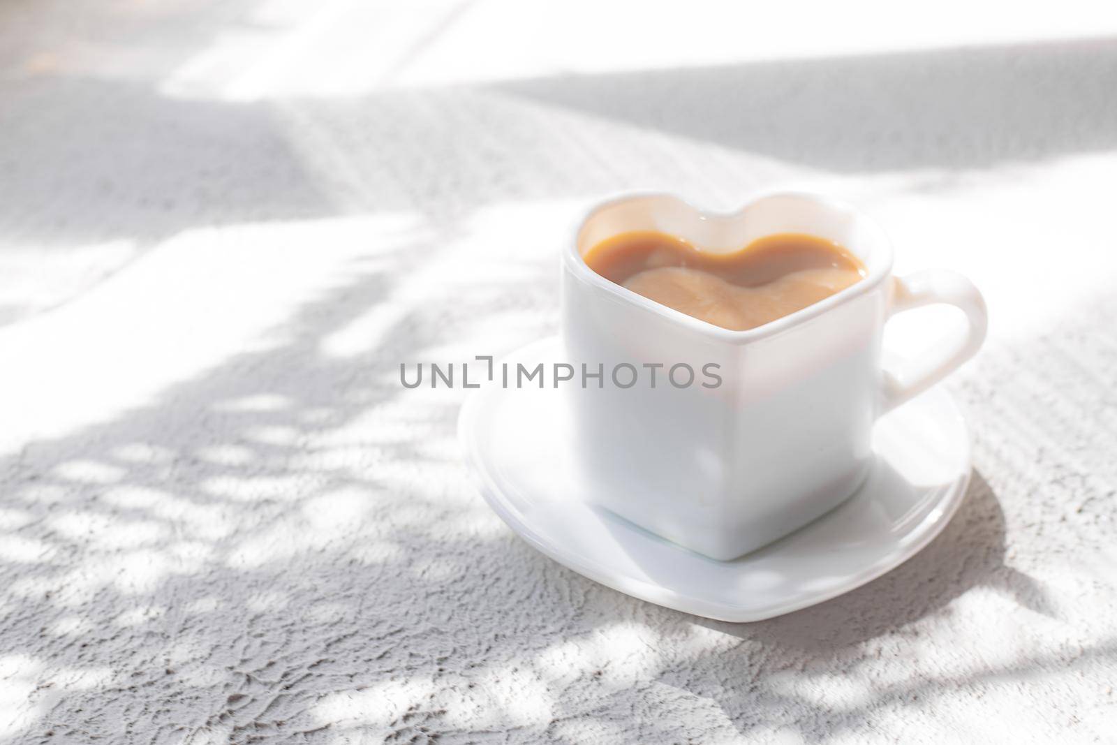 A cup of cappuccino on a saucer and shade from the sun. Coffee drink. Copy space. A heart-shaped cup. Relax