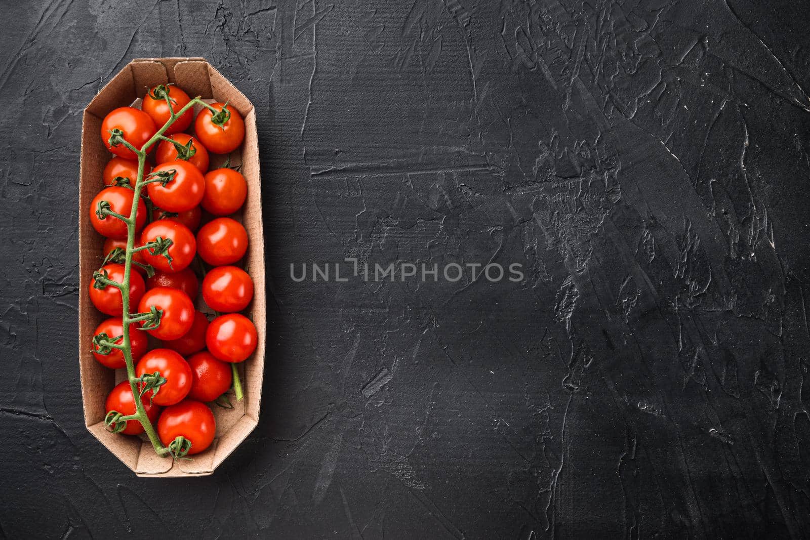 Cherry tomatoes on branch set, in container, on black stone background, top view flat lay, with copy space for text