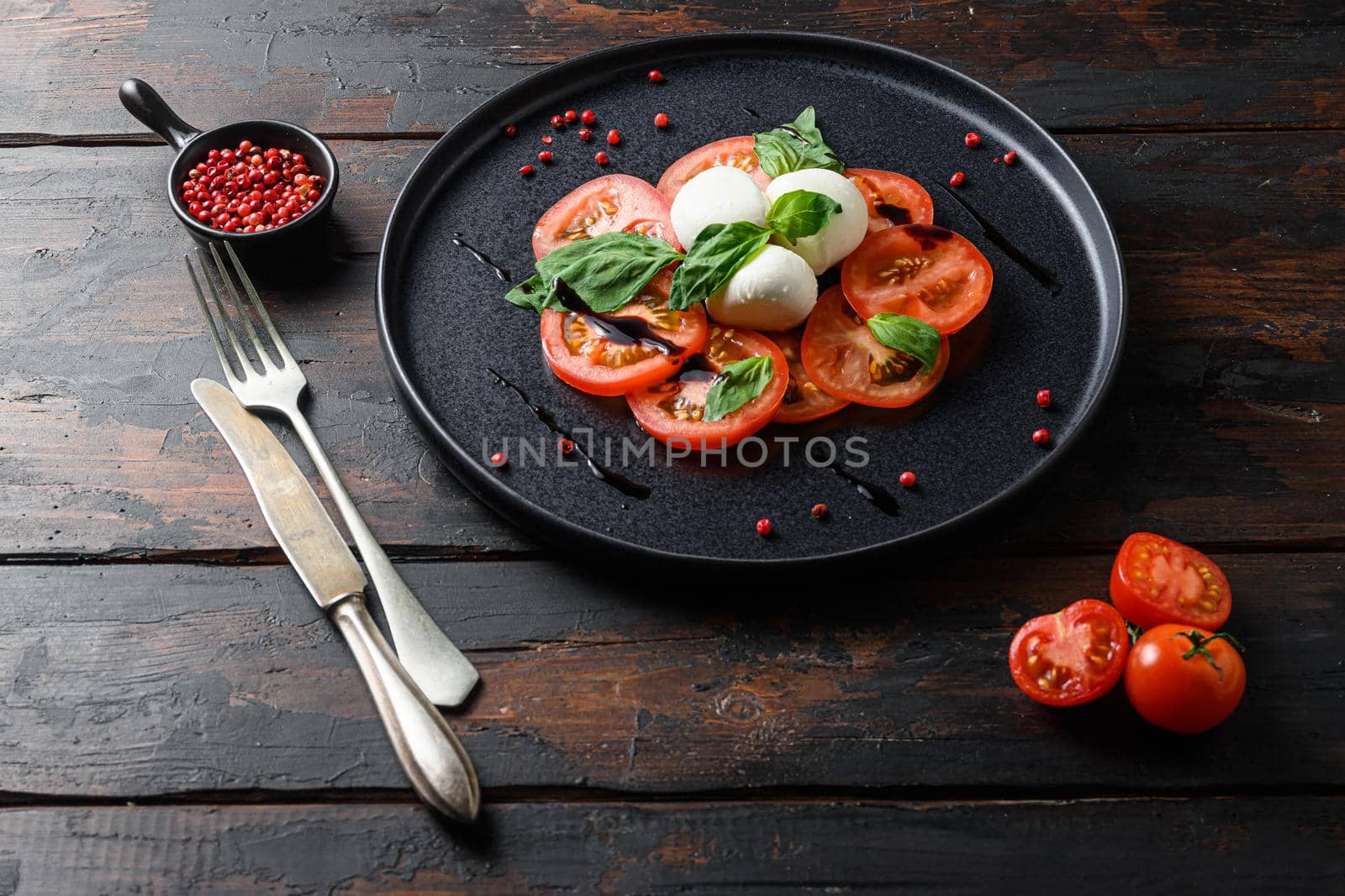 Caprese salad Tomato and mozzarella slices with basil leaves on olive wood dark table .