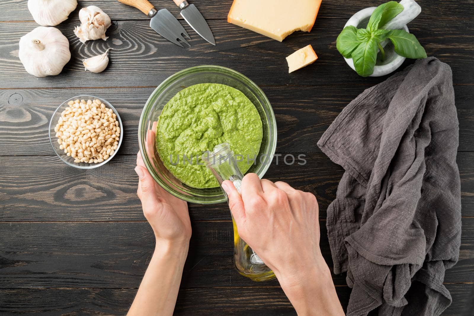 Italian Cuisine. Step by step cooking italian pesto sauce. Step 7 - adding some olive oil. Fresh green basil, parmesan cheese, nuts, olive oil and garlic top view on black wooden table