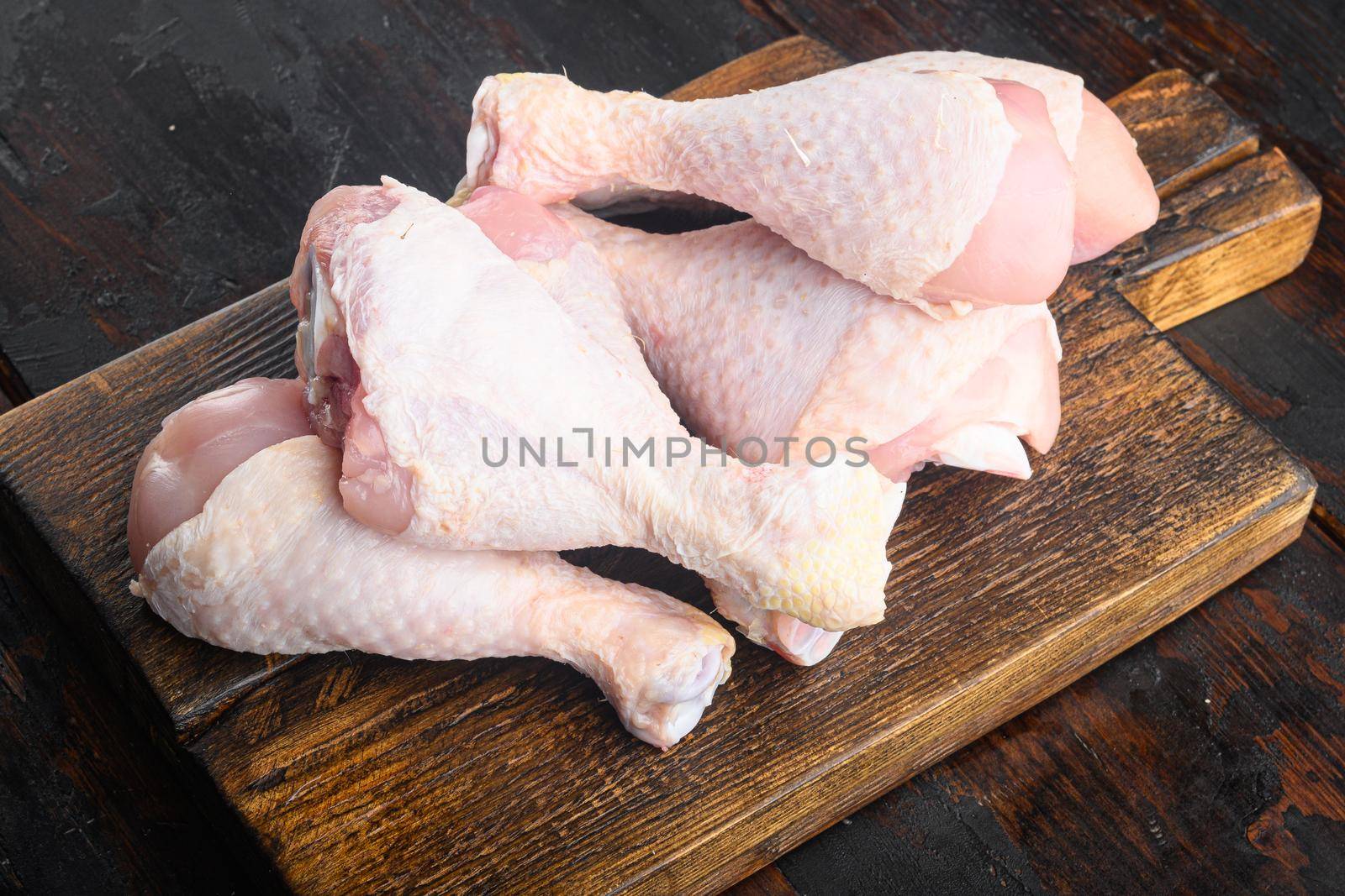 Primal cut of raw chicken legs, with chicken thighs and drumsticks set, on wooden cutting board, on old dark wooden table