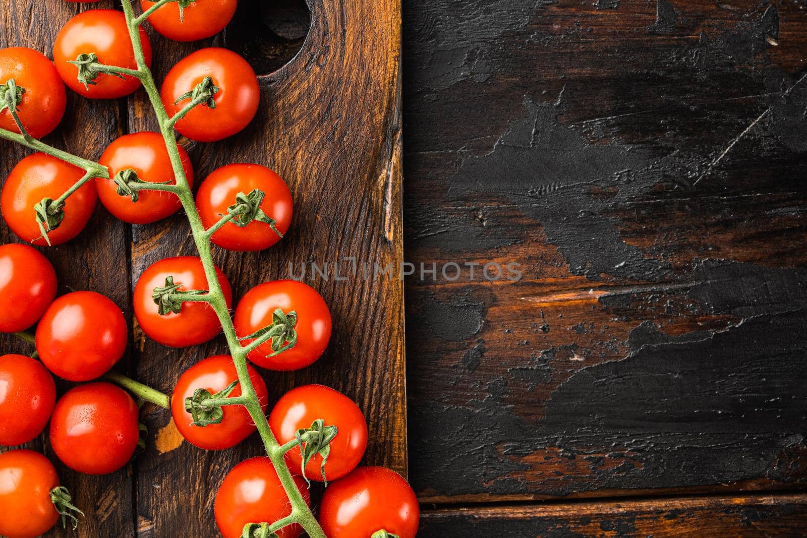 Fresh ripe cherry tomatoes set, on wooden cutting board, on old dark wooden table background, top view flat lay, with copy space for text
