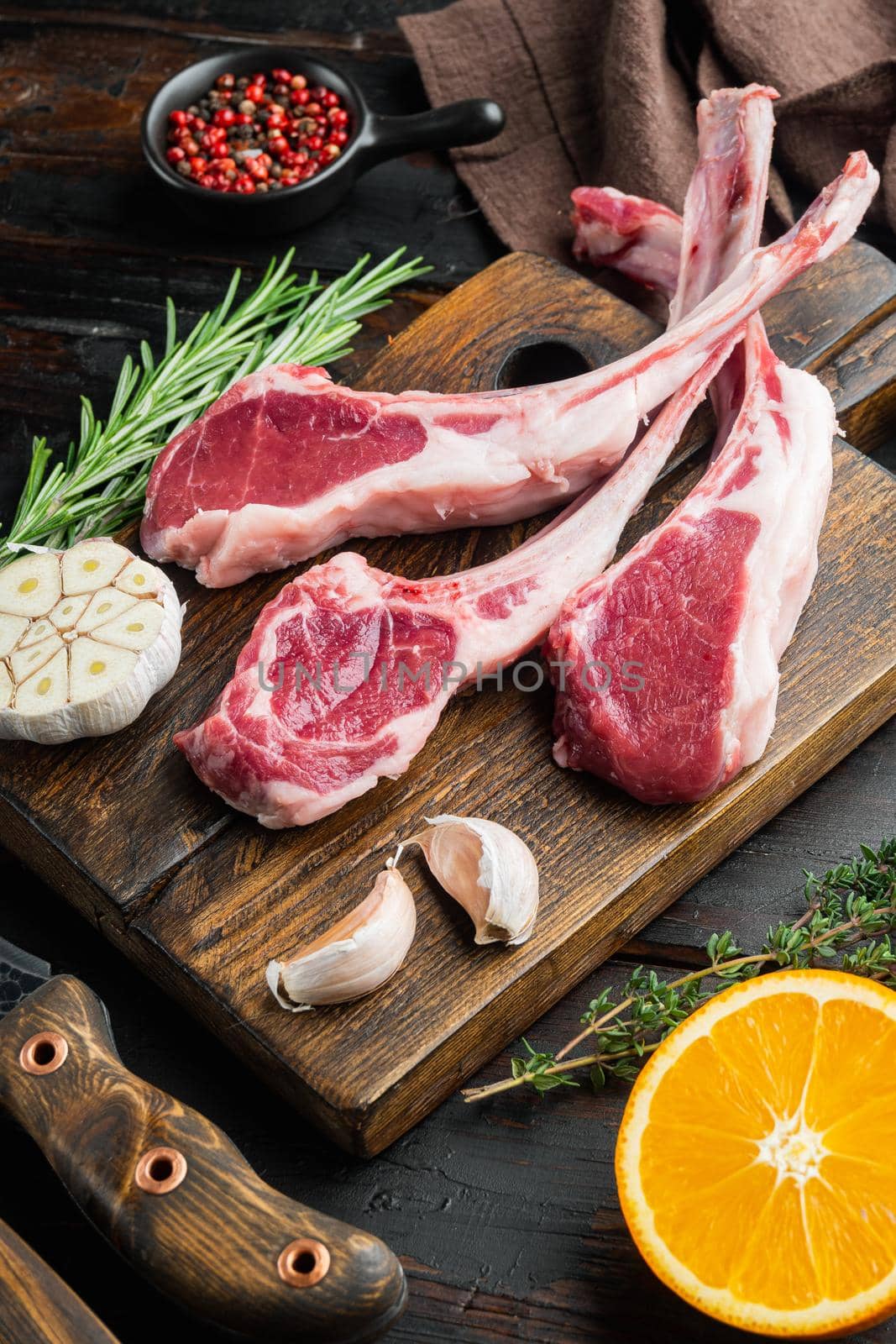 Frenched raw fatty lamb chops set, with ingredients carrot orange, herbs, on old dark wooden table background