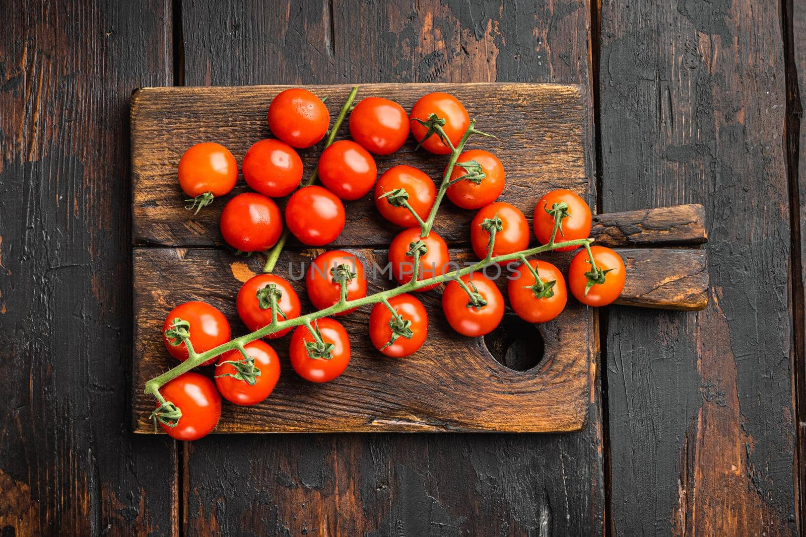 Cherry tomatoes on branch set, on wooden cutting board, on old dark wooden table background, top view flat lay
