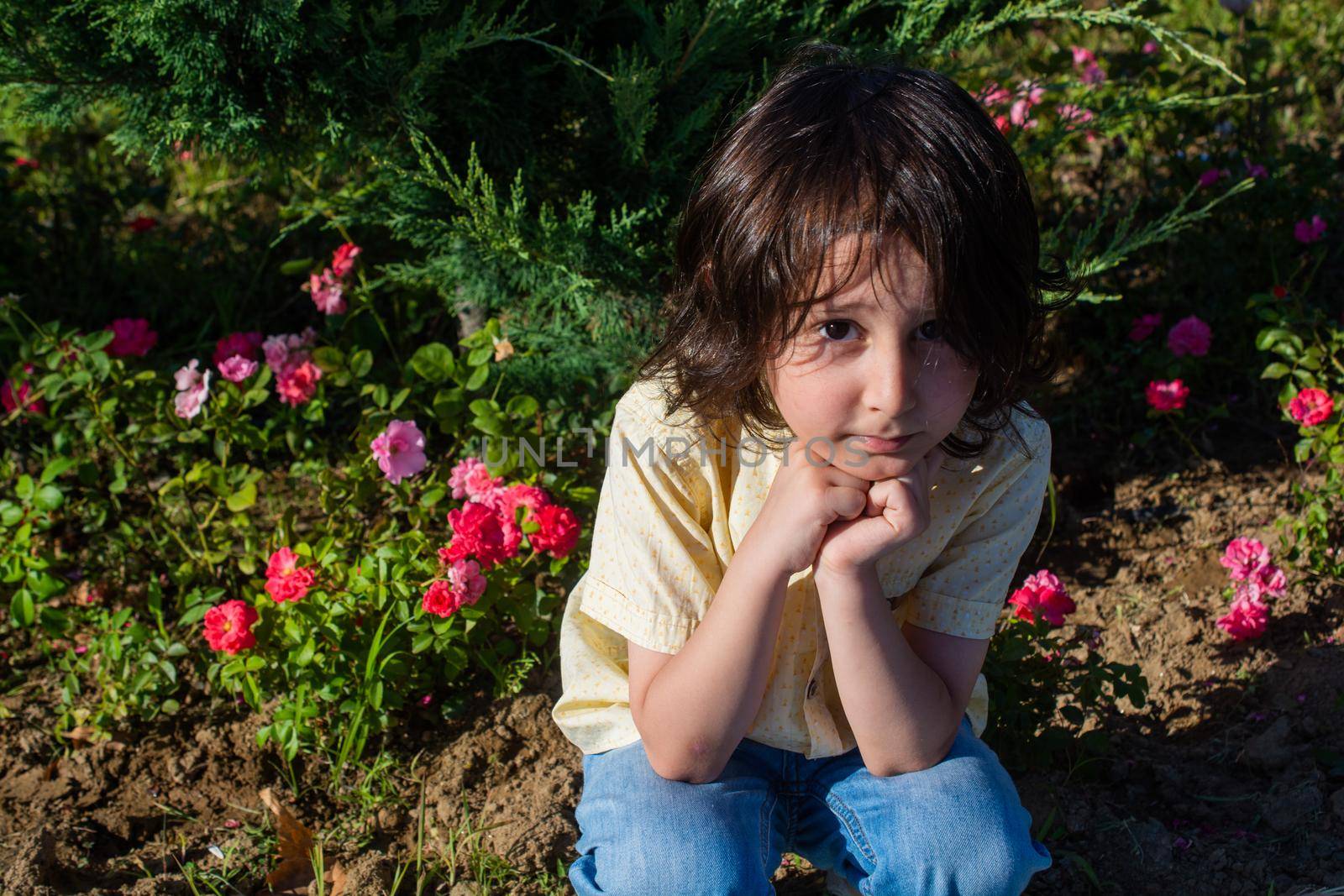 View of thoughtful cute little  boy in a rose flower garden