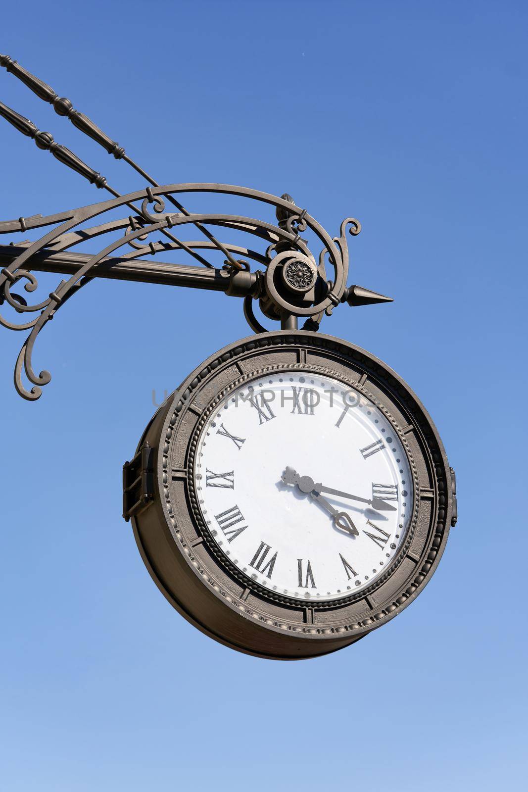 Antique round clock with Roman numerals hang on the street of the city. Close up