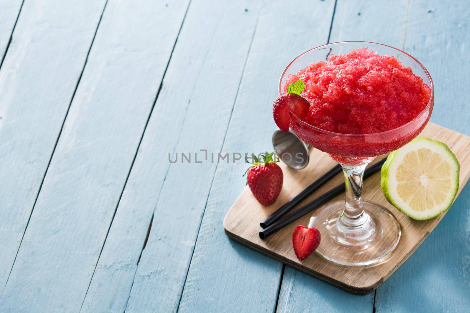 Strawberry margarita cocktail in glass on blue wooden table