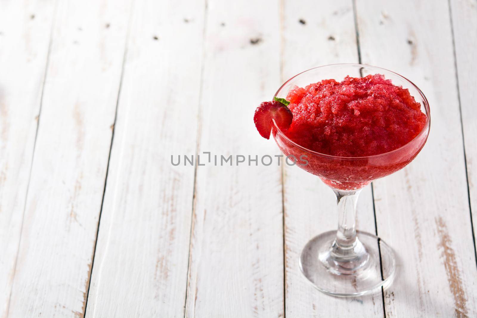 Strawberry margarita cocktail in glass on white wooden table.